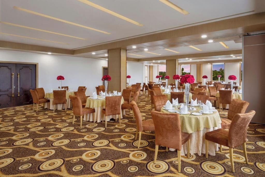 A hotel dining area with round tables, brown chairs, and red flower centerpieces.