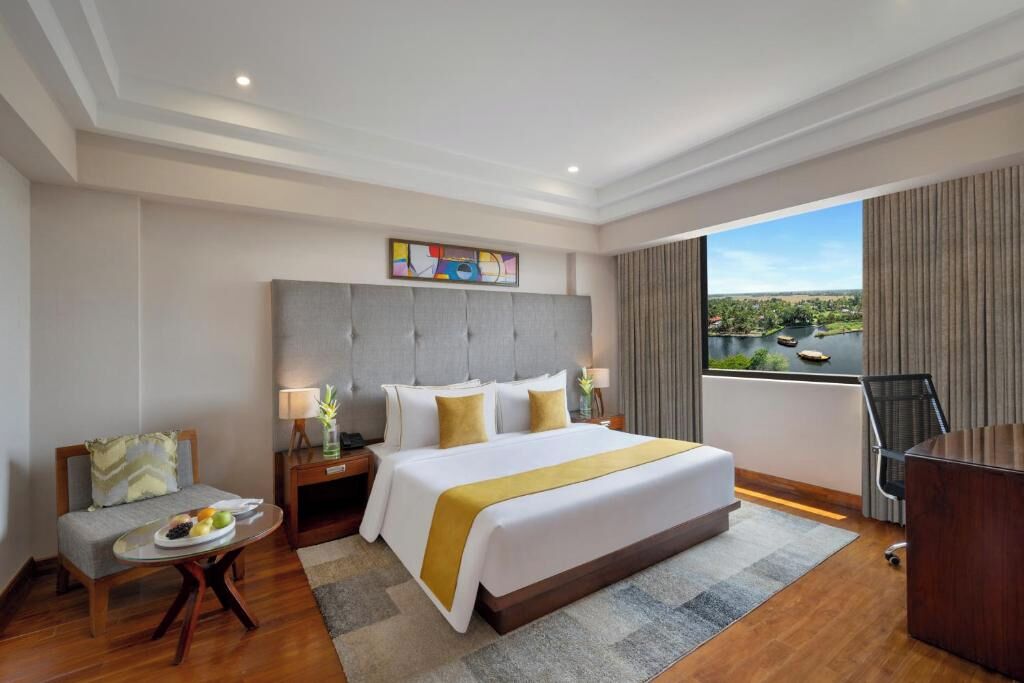Habitación de hotel con una cama grande, un escritorio, una silla, una mesita con fruta y vista al río.