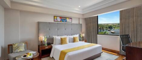 Habitación de hotel con una cama grande, un escritorio, una silla, una mesita con fruta y vista al río.