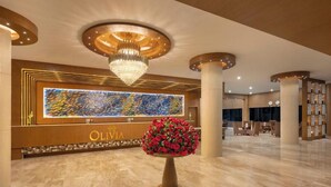 A hotel reception area with a large, illuminated wall art piece, a chandelier, and a floral centerpiece. - Olivia Alleppey (Alappuzha)