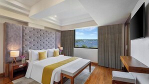 A hotel room with a large bed, a TV, a desk, and a view of the sea. - Olivia Alleppey (Alappuzha)