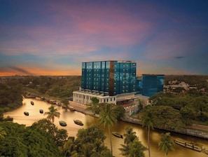 A modern hotel with a glass facade, situated by a river with boats.