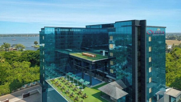 A modern hotel with a glass facade, outdoor pool, and a view of the water. - Olivia Alleppey (Alappuzha)