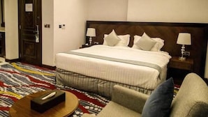 Une chambre d’hôtel avec un grand lit, deux lampes de chevet, une moquette à motifs et une petite table avec une télécommande.