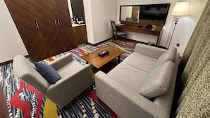Une chambre d’hôtel équipée d’un canapé, d’un fauteuil, d’une télévision, d’un bureau et d’une moquette à motifs.