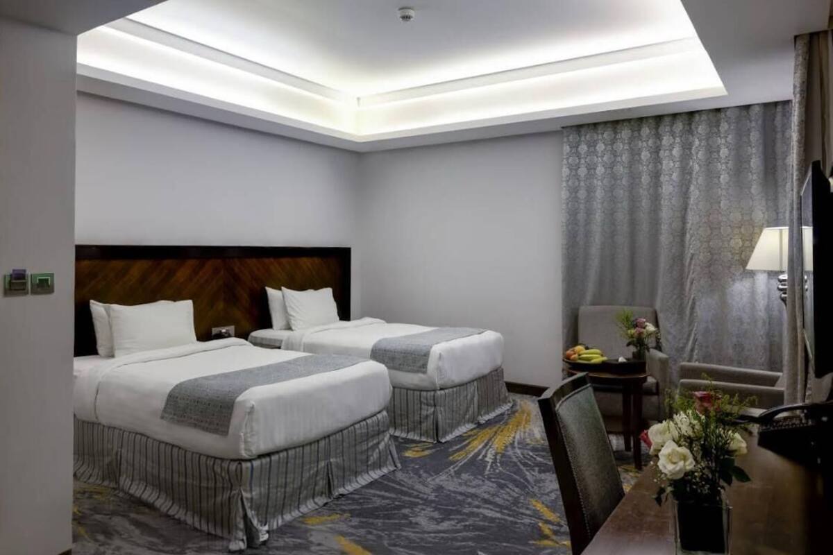A hotel room with two beds, a desk, a chair, a TV, and a window with curtains.