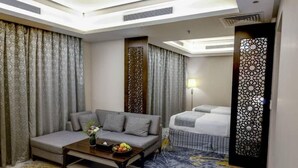 Une chambre d’hôtel avec un canapé, un lit, une table basse avec des fruits et un paravent décoratif.