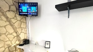 A room with a stone wall, a mounted TV, a white table with chairs, a tripod, and a shelf. - Studio Montorgueil Paris 2 (Paris)