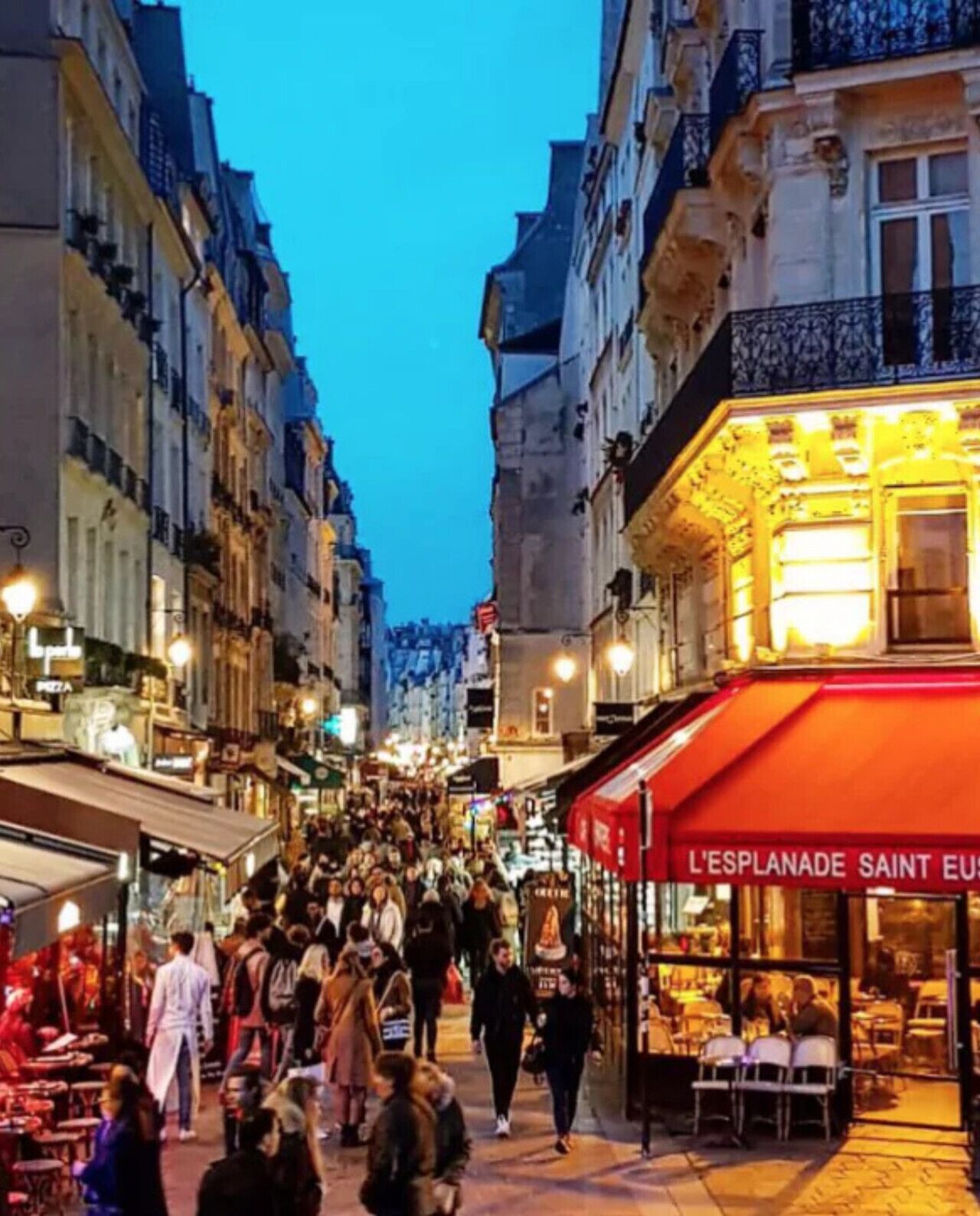A bustling street scene with people walking and shops on either side.