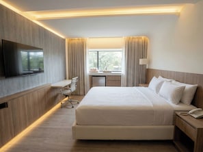 Una habitación de hotel con cama, escritorio, silla, televisor y ventana con cortinas.