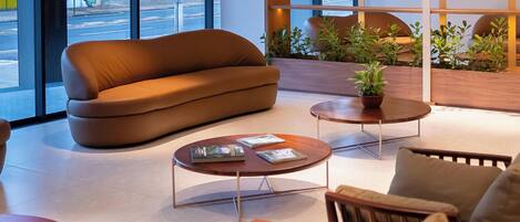 Un intérieur moderne avec un canapé, deux tables basses et un coin salon offrant une vue sur la rue.