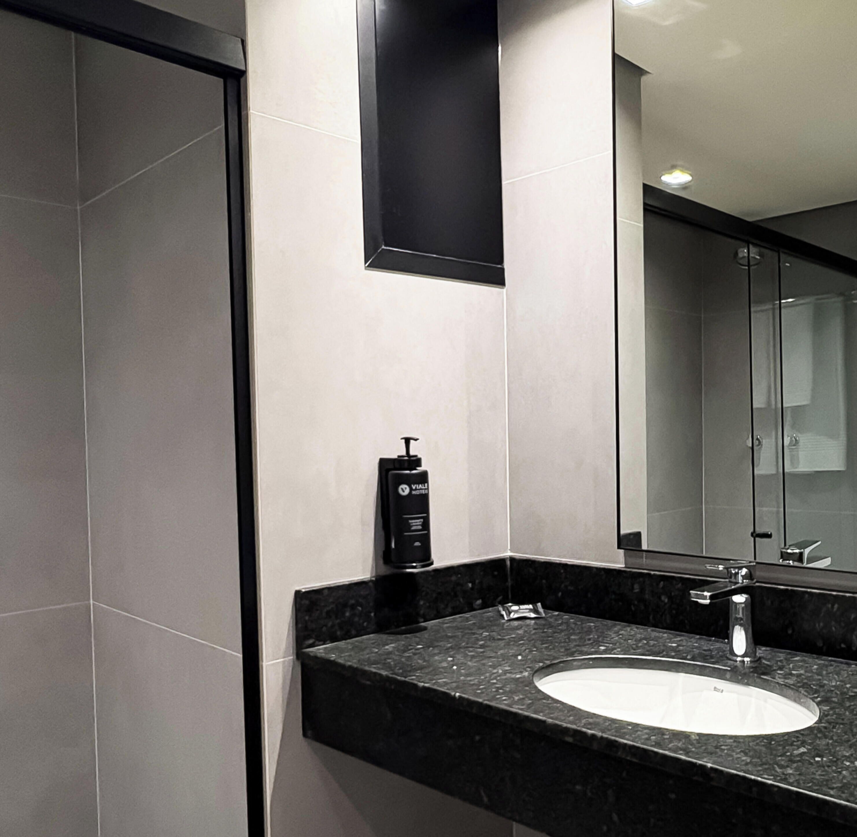 A modern bathroom with a marble countertop, a white sink, a black soap dispenser, and a large mirror.
