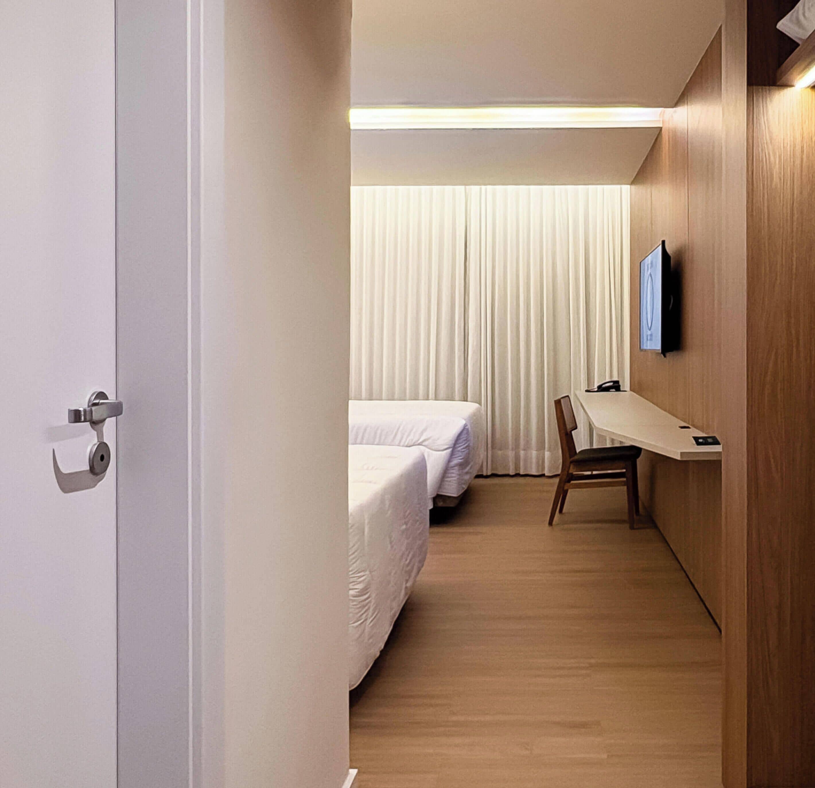 Une chambre d’hôtel avec un plancher en bois, un bureau avec une chaise, un lit et un téléviseur fixé au mur.