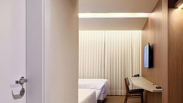 Habitación de hotel con piso de madera, un escritorio con silla, una cama y un televisor montado en la pared.