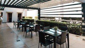 An outdoor dining area with tables and chairs, a pergola overhead, and a view of the city skyline. - City-View + Spacious Unit | Across Trinoma Mall (Quezon City)
