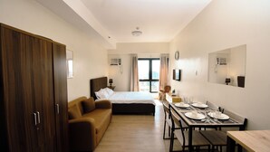 A bedroom with a bed, a sofa, a desk with chairs, and a dining table set for four. - City-View + Spacious Unit | Across Trinoma Mall (Quezon City)