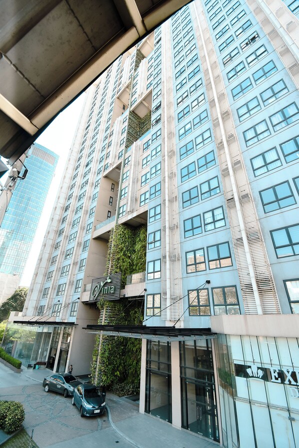 A high-rise building with multiple balconies, a glass facade, and a parking area with cars. - City-View + Spacious Unit | Across Trinoma Mall (Quezon City)