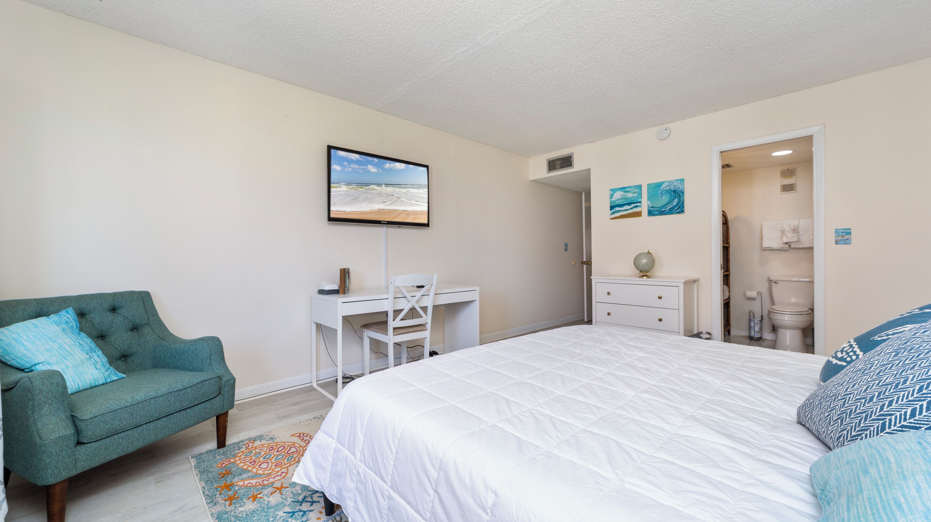 A bedroom with a bed, a desk, a chair, a couch, and a bathroom visible through an open door.