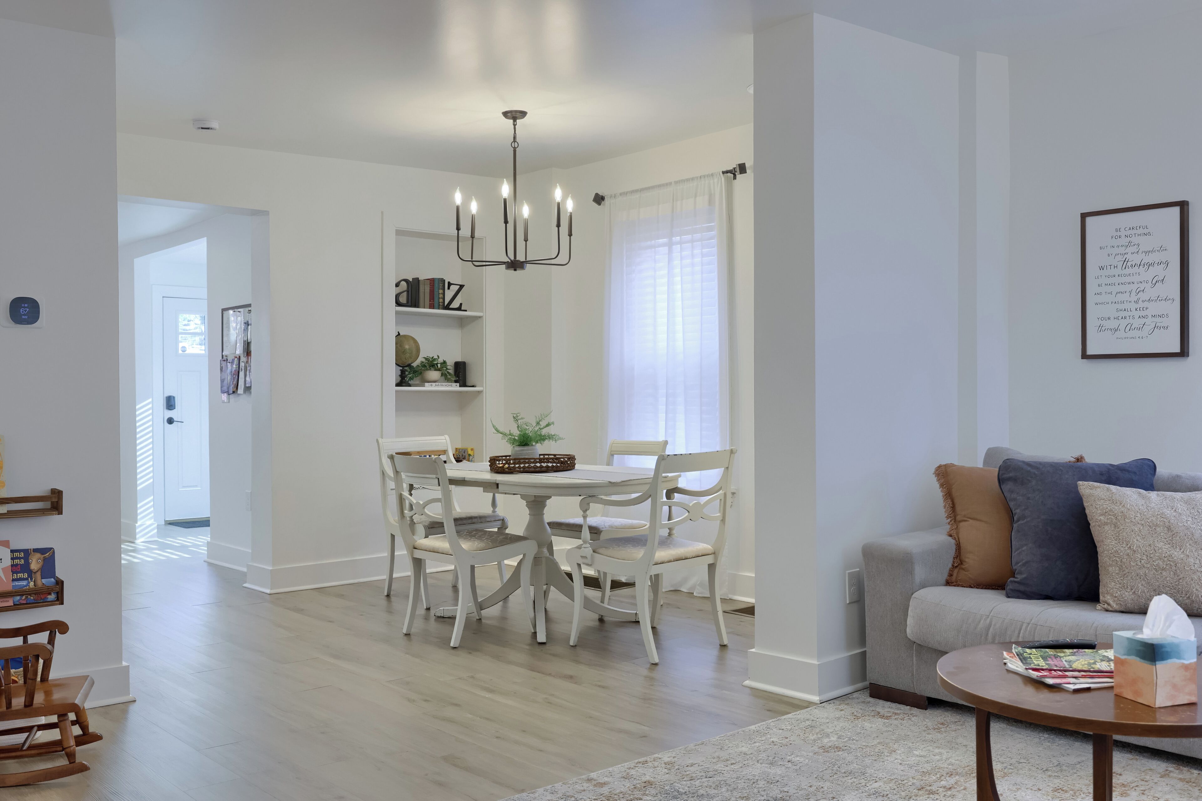 A modern living room with a grey sofa, a coffee table, and a dining area with a white table and chairs.