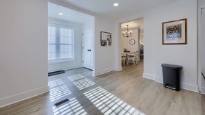 A spacious hallway with a dining area in the background, a trash bin, and a wall-mounted clock. - Hot Tub Retreat Between Philly & Lancaster (Parkesburg)
