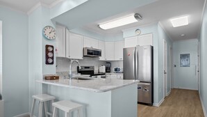 A modern kitchen with white cabinetry, stainless steel appliances, and a marble countertop. - Dune Daze-Ocean Front Condo in Dunescape Villas (Atlantic Beach)