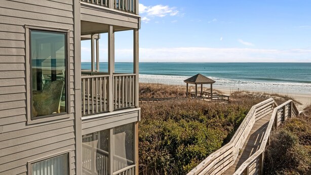 A coastal building with a balcony overlooking the beach, a wooden deck, and a beach gazebo. - Dune Daze-Ocean Front Condo in Dunescape Villas (Atlantic Beach)