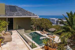 A modern house with a swimming pool, outdoor seating, and a view of the sea. - Luxury Camps Bay 5 Star w Gym Pool Kinvara Villa (Cape Town)