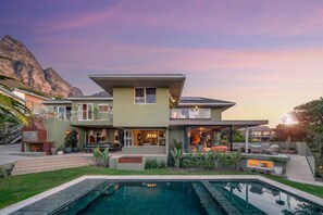 A modern two-story house with a pool, outdoor seating, and a mountain backdrop. - Luxury Camps Bay 5 Star w Gym Pool Kinvara Villa (Cape Town)