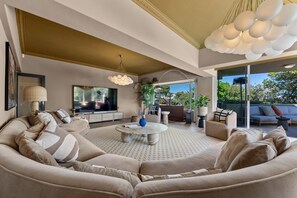 A modern living room with a large sectional sofa, a television, and a dining area with a round table. - Luxury Camps Bay 5 Star w Gym Pool Kinvara Villa (Cape Town)
