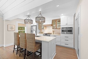 A modern kitchen with a central island, stainless steel appliances, and wicker chairs. - Seaside Oaks-Pet Friendly/Oceanside Home (Atlantic Beach)