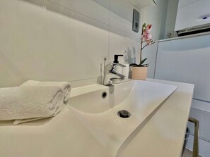 A modern bathroom with a white sink, a towel, a potted plant, and a wall-mounted air conditioning unit. - Suite in Antwerp Near Meir Shops (Antwerp)