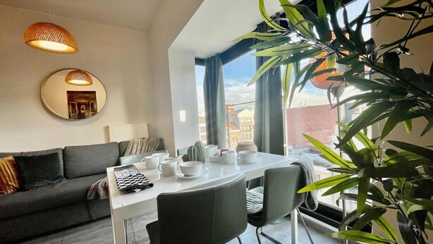 A modern living room with a dining area, large windows, and a plant. - Suite in Antwerp Near Meir Shops (Antwerp)