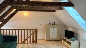 A loft bedroom with exposed wooden beams, a green sofa, a white rug, a TV on a cabinet, and a bed with a green cover. - Ferienwohnung im Herzen Goslars mit Blick auf die Marktkirche  (Goslar)