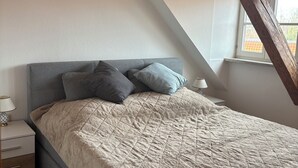 A bedroom with a bed, bedside table, lamp, and a window with a view of the outside. - Ferienwohnung im Herzen Goslars mit Blick auf die Marktkirche  (Goslar)