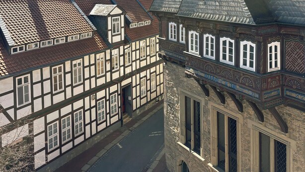 A traditional half-timbered building with a steeply pitched roof, a narrow street, and a mountain in the background. - Ferienwohnung im Herzen Goslars mit Blick auf die Marktkirche  (Goslar)