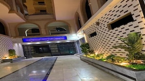 L’entrée d’un hôtel, avec une façade moderne, un chemin central et une enseigne indiquant le nom de l’hôtel.