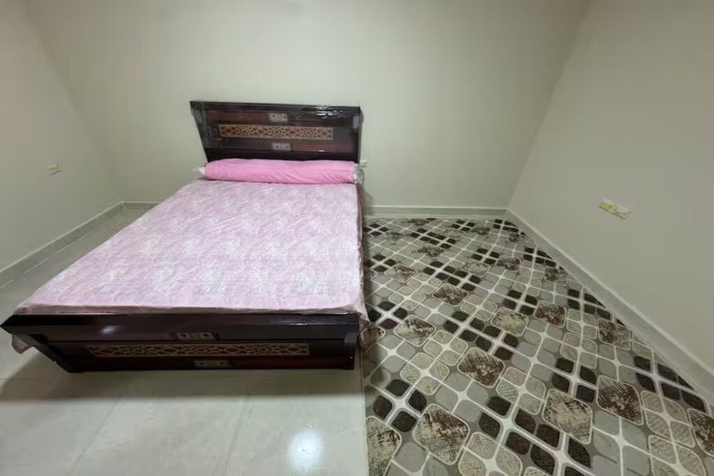 A small room with a bed, a tiled floor, and a plain wall.