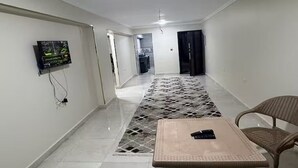 Un couloir avec un sol carrelé, un téléviseur fixé au mur, un tapis à motifs et une chaise.