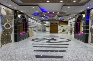 En hall med en central, cirkelformad design i golvet, väggar med dekorativa mönster och ett tak med infälld belysning och en central kristallkrona.