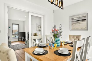 Un coin repas avec une table en bois, des chaises blanches et un vase rempli de fleurs.
