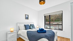 Quarto com cama, mesas de cabeceira, janela com vista e luminária no teto.