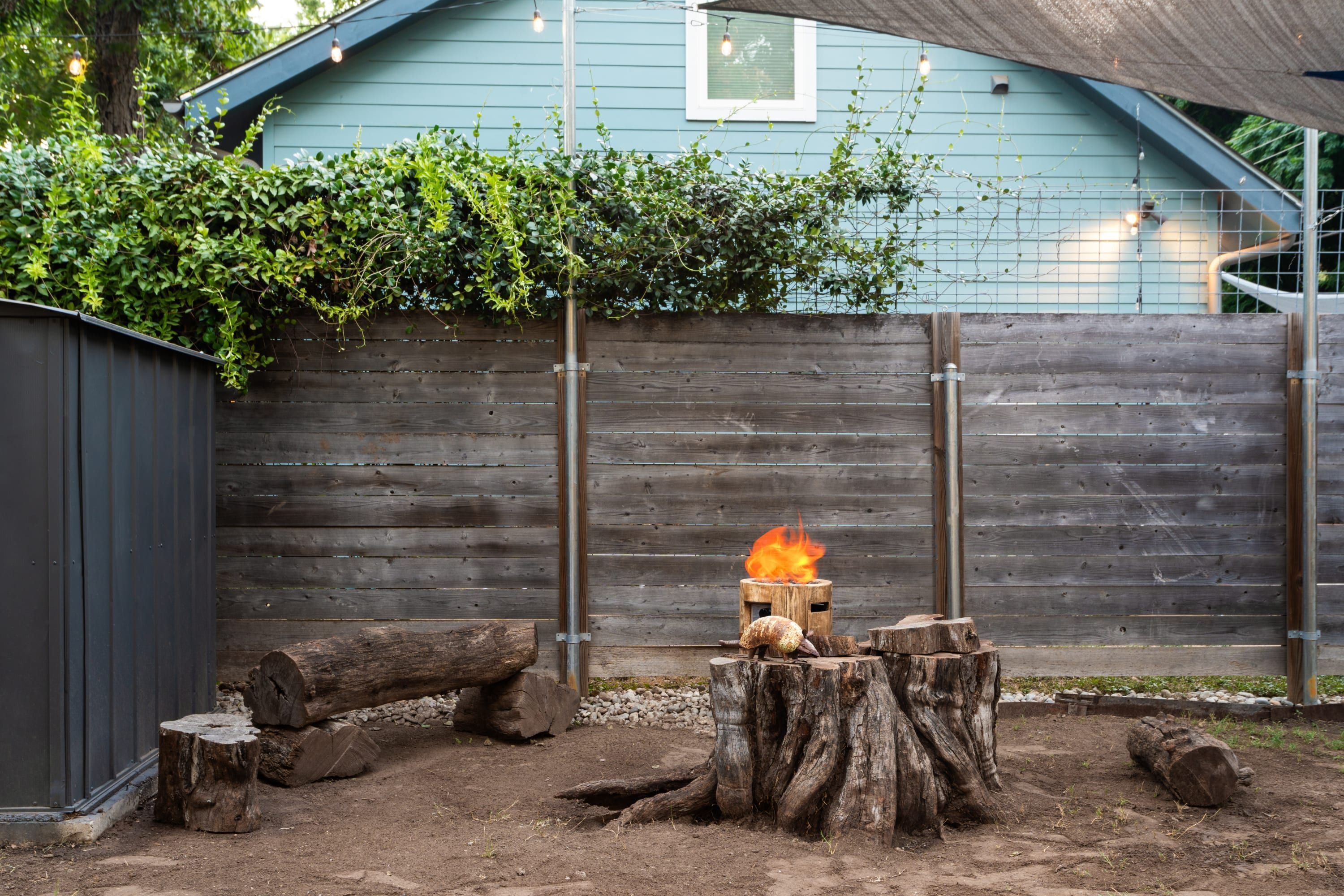 A backyard with a fire pit, wooden fence, and a blue building in the background.