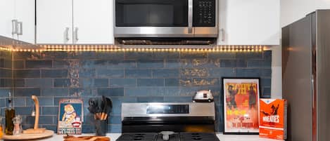 A kitchen with a microwave, stove, and refrigerator, featuring a blue brick backsplash and white cabinetry.
