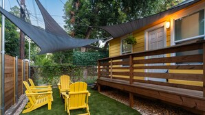 A fenced backyard with artificial grass, wooden deck, and Adirondack chairs. - East Austin Bungalow w BBQ Firepit Fun Yard (Austin)