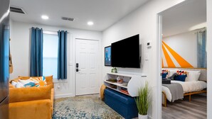 A modern living room with a flat-screen TV, a sofa, a coffee table, and a bed with a striped headboard. - East Austin Bungalow w BBQ Firepit Fun Yard (Austin)