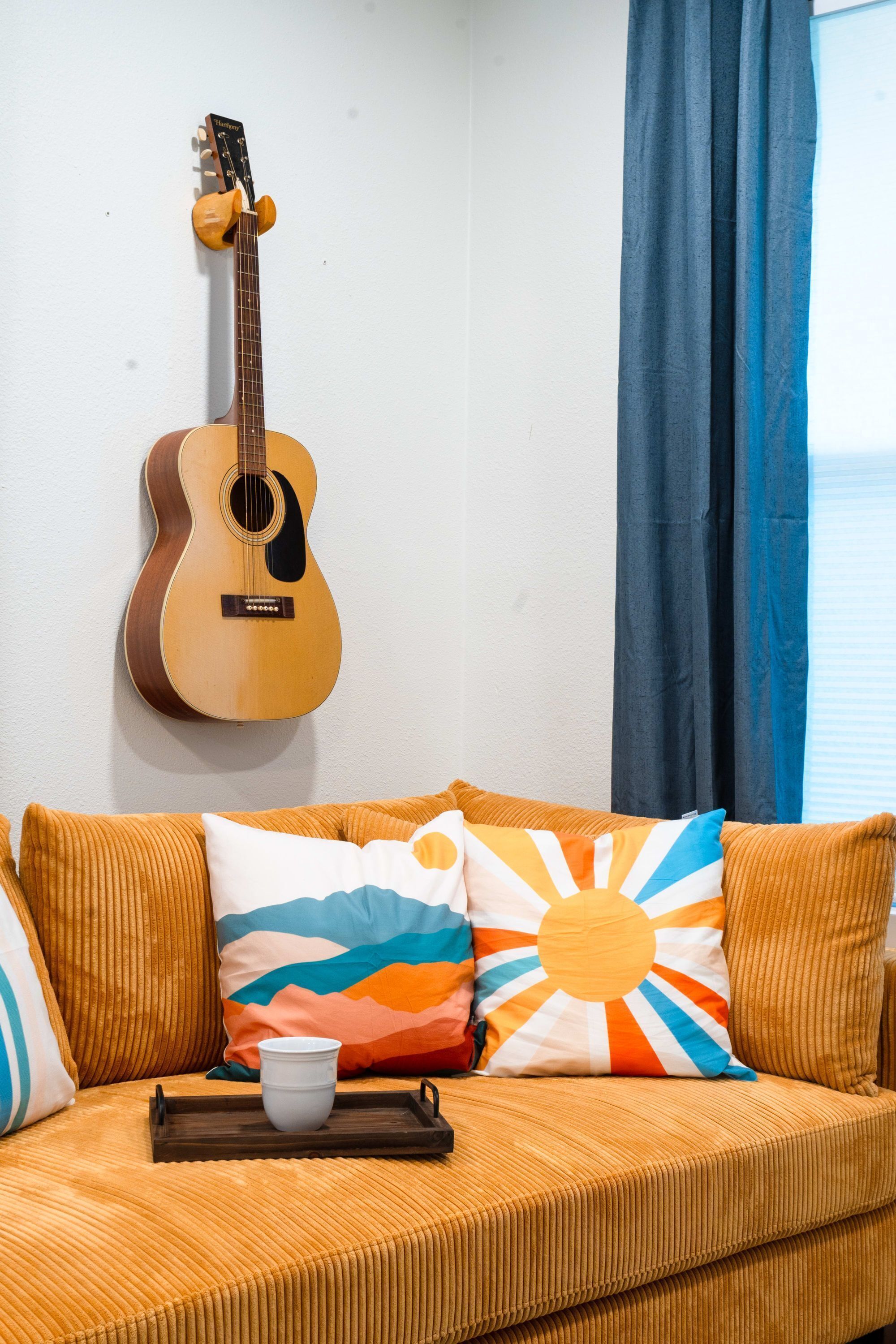 Une pièce dans laquelle on peut voir une guitare accrochée au mur, un canapé agrémenté de coussins colorés et une table basse sur laquelle se trouve une tasse.