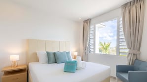 A hotel room with a bed, a nightstand, a chair, and a window with curtains. - Aquamarine at Blue Bay Beach Golf Resort (Sint Michiel)