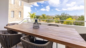 A wooden table with wicker chairs on a balcony with a clear view of the sky and surrounding vegetation. - Aquamarine at Blue Bay Beach Golf Resort (Sint Michiel)