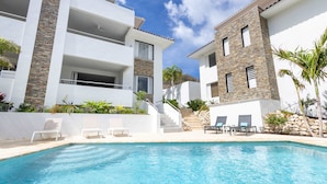 A modern building with a swimming pool, white balconies, and stone accents. - Aquamarine at Blue Bay Beach Golf Resort (Sint Michiel)