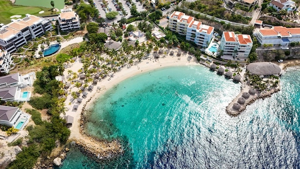 An aerial view of a coastal resort with beachfront properties, a sandy beach, and clear turquoise waters. - Aquamarine at Blue Bay Beach Golf Resort (Sint Michiel)